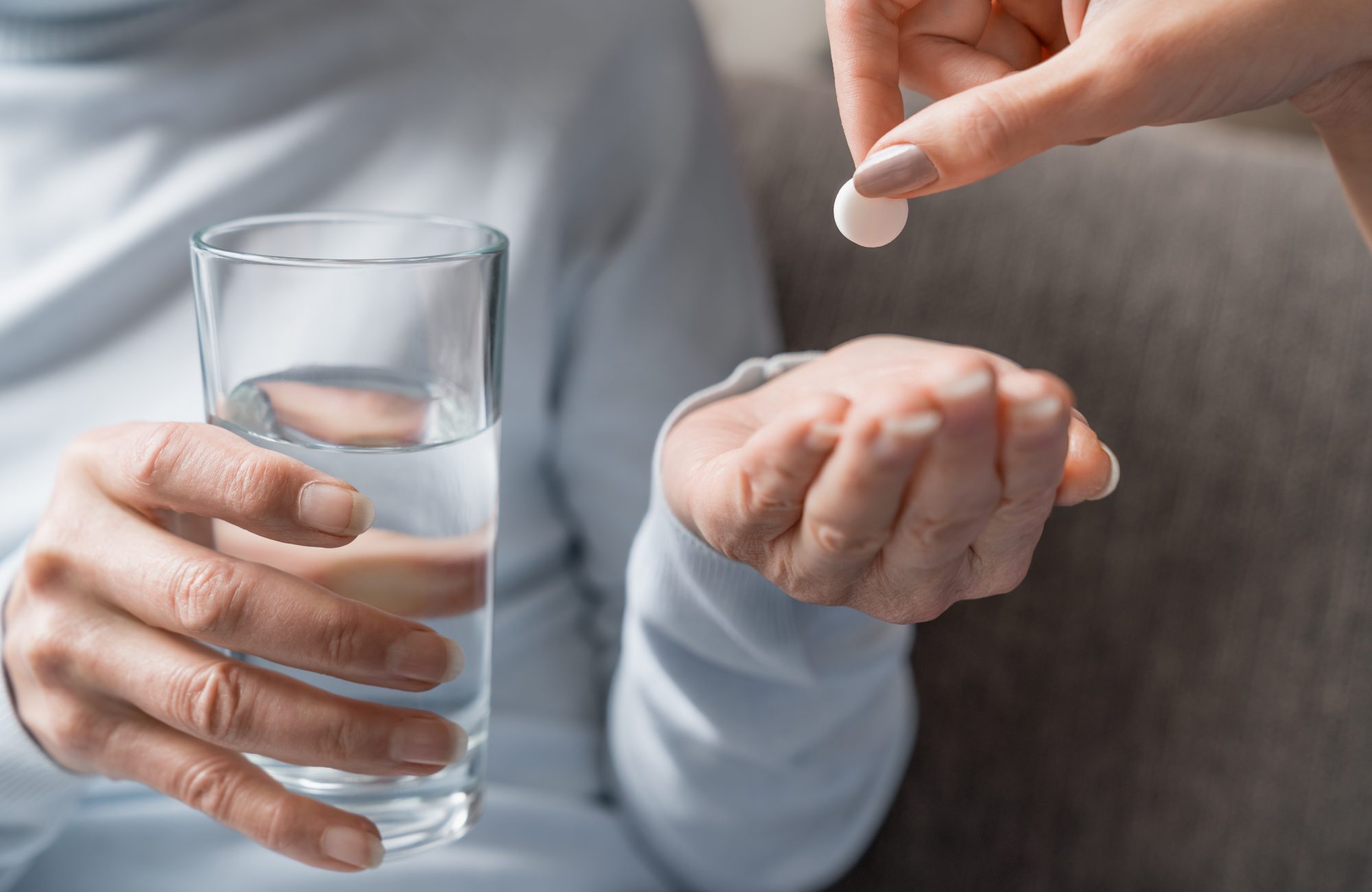 Caring nurse giving pills to senior woman with glass of water in hand